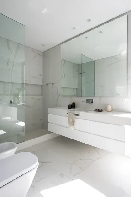Baño moderno con revestimientos de mármol y vanitory flotante — proyecto Casa AA, por Estudio Junor, en Pilar